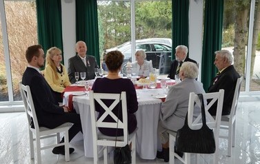 Zdjęcie przedstawia jubilat&oacute;w siedzących przy okrągłym stole. Wraz z nimi znajduje się w&oacute;jt oraz przewodnicząca rady.