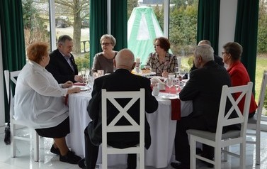 Zdjęcie przedstawia jubilat&oacute;w siedzących przy okrągłym stole. Rozmawiają ze sobą. 
