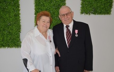 Zdjęcie przedstawia pare jubilat&oacute;w. Kobieta w kr&oacute;tkich włosach oraz w białej bluzce, mężczyzna w ciemnym garniturze, ma okulary.