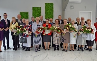 Zdjęcie przedstawia zdjęcie grupowe wszystkich par obchodzących jubileusz wraz z w&oacute;jtem, przewodniczącą rady i kierownikiem USC.