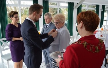 Na zdjeciu w&oacute;jt przypina medal kobiecie w jasnej garsonce. Obok stoi mąż oraz przewodnicząca Rady Gminy. Na zdjęciu plecami odwr&oacute;cona jest kierownik Urzędu Stanu Cywilnego w czerwonej garsonce.
