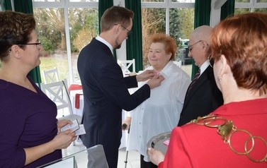 Na zdjęciu w&oacute;jt przypina kobiecie medal. Jest ona uśmiechnięta. Obok stoi mąż.