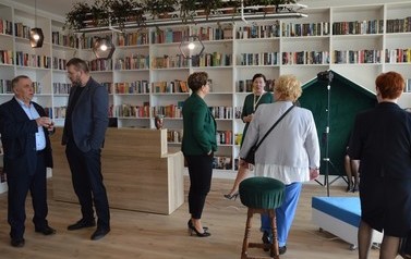 Na zdjęciu ludzie podziwiają nowowczesne wnętrze biblioteki. Białe p&oacute;łki z książkami. 