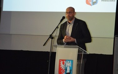 Zdjęcie przedstawia meżczyznę wygłaszającego przemowę.