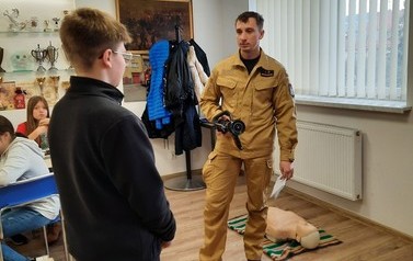 Chłopiec stojący bokiem do męzczyzny ubranego w str&oacute;j strażaka i trzymający prądownice w ręku