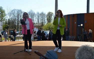 Na zdjęciu znajdują się dwie kobiety stojące na scenie amfiteatru. W rękach trzymają mikrofony. 
