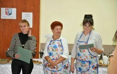  Trzy kobiety, jedna ubrana elegancko a pozostałe kobiety mają na sobie fartuch. 