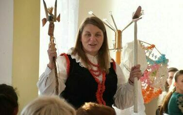 Kobieta ubrana w str&oacute;j pałucki pokazuje zebranym dwa dawne symbole pałuckie. Drewniane patyki przedstawiają bociana i kozła.