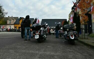 Tyły motocykl&oacute;w oraz grupa mężczyzn ubrana na czarno znajdujących się przy swoich maszynach.