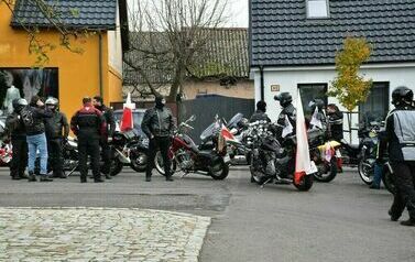 Grupa mężczyzn, za kt&oacute;rymi znjadują się motocyke. Przypięte do nich zostały flagi polski.