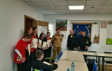 Grupa dziewczyn z dyplomami w ręku stoi wraz z trzema strażakami