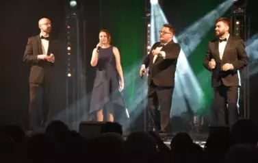 widzimy trzech pan&oacute;w i panią śpiewających na scenie 