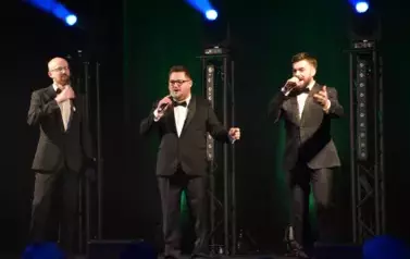 widzimy trzech pan&oacute;w śpiewających na scenie