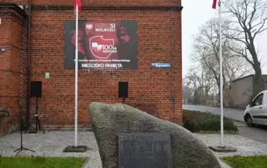 widzimy pomnik ozdobiony pięknymi bukietami oraz dwoma zniczami