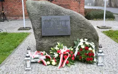 widzimy pomnik ozdobiony pięknymi bukietami oraz dwoma zniczami