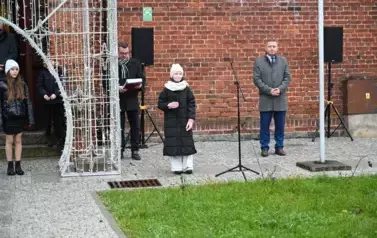 widzimy dziewczynkę m&oacute;wiącą do mikrofonu oraz kilka os&oacute;b stojących obok 