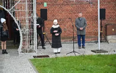 widzimy dziewczynkę m&oacute;wiącą do mikrofonu oraz kilka os&oacute;b stojących obok 