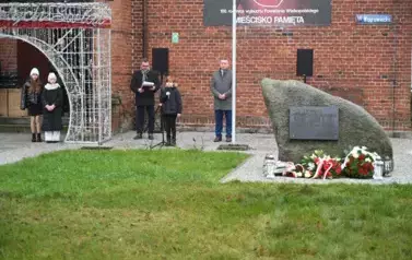 widzimy chłopca m&oacute;wiącego do mikrofonu oraz kilka os&oacute;b stojących obok 