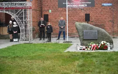 widzimy chłopca m&oacute;wiącego do mikrofonu oraz kilka os&oacute;b stojących obok 