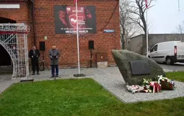 widzimy pana m&oacute;wiącego do mikrofonu oraz pomnik