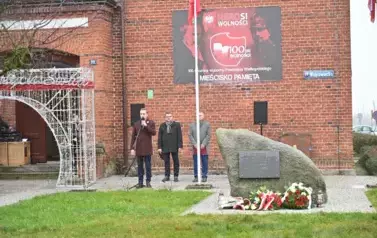 widzimy stojących za pomnikiem trzech pan&oacute;w