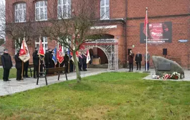 widzimy delegacje sztandarowe, pomnik oraz stojących za pomnikiem trzech pan&oacute;w