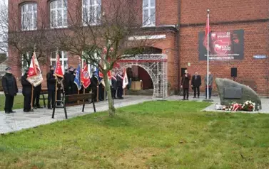 widzimy delegacje sztandarowe, pomnik oraz stojących za pomnikiem trzech pan&oacute;w