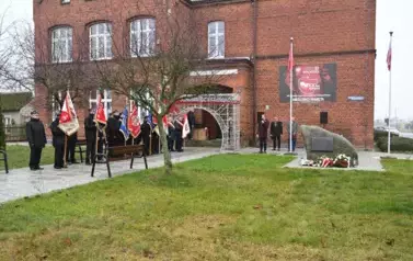 widzimy delegacje sztandarowe, pomnik oraz stojących za pomnikiem trzech pan&oacute;w