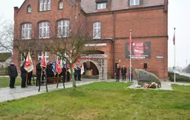widzimy delegacje sztandarowe, pomnik oraz stojących za pomnikiem trzech pan&oacute;w
