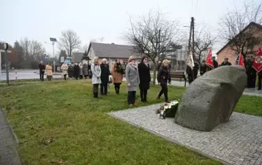 widzimy trzy osoby stojące przed pomnikiem