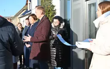 widzimy liczną grupę os&oacute;b oraz dwie panie trzymające niebieską wstęge