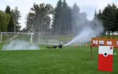 Zawodnicy drużyny w zadaniu imitacji akcji gaśniczej strącający pachołki wodą