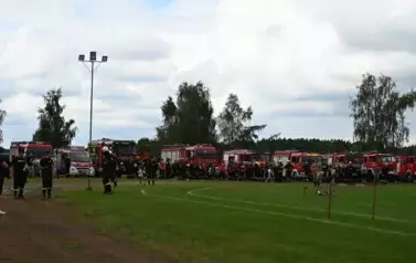 Strażacy stojący obok swoich woz&oacute;w strażackich