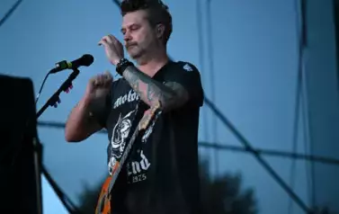widzimy pana trzymającego dłonie w g&oacute;rze oraz posiadającego na pasku gitarę 