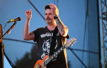 widzimy pana trzymającego dłonie w g&oacute;rze oraz posiadającego na pasku gitarę 