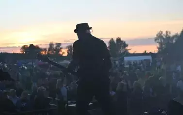 widzimy grającego gitarzystę na tle widowni i zachodu słońca
