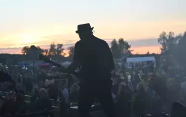 widzimy grającego gitarzystę na tle widowni i zachodu słońca