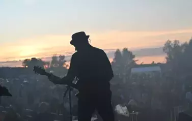 widzimy grającego gitarzystę na tle widowni i zachodu słońca