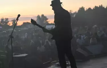 widzimy grającego gitarzystę na tle widowni i zachodu słońca