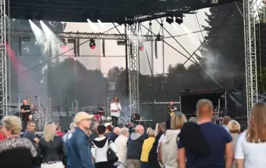 widzimy grupę os&oacute;b słuchającą koncertu a w tle zesp&oacute;ł muzyczny