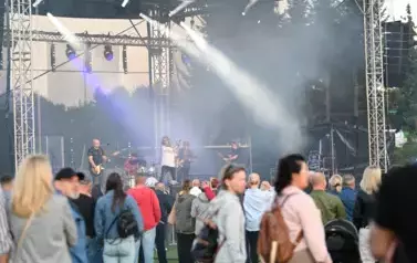 widzimy grupę os&oacute;b słuchającą koncertu a w tle zesp&oacute;ł muzyczny