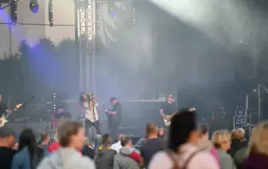 widzimy grupę os&oacute;b słuchającą koncertu a w tle zesp&oacute;ł muzyczny