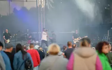 widzimy grupę os&oacute;b słuchającą koncertu a w tle zesp&oacute;ł muzyczny