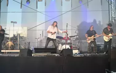 widzimy wokalistę, dw&oacute;ch pan&oacute;w grających na gitarze oraz pana grającego na perkusji