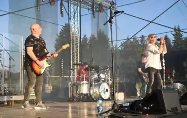 widzimy dw&oacute;ch pan&oacute;w grających na gitarze, śpiewającego wokalistę oraz pana grającego na perkusji