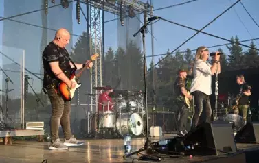 widzimy trzech pan&oacute;w grających na gitarze, śpiewającego wokalistę oraz pana grającego na perkusji