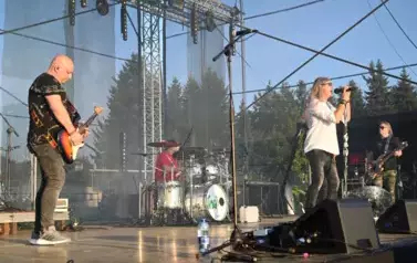 widzimy dw&oacute;ch pan&oacute;w grających na gitarze, śpiewającego wokalistę oraz pana grającego na perkusji