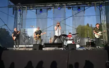 widzimy trzech pan&oacute;w grających na gitarze, śpiewającego wokalistę oraz pana grającego na perkusji