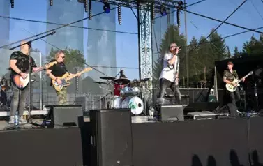 widzimy trzech pan&oacute;w grających na gitarze oraz śpiewającego wokalistę