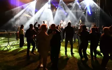 widzimy grupę os&oacute;b stojących pod sceną, na kt&oacute;rej występuje zesp&oacute;ł